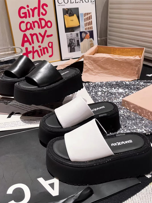 Two pairs of women's platform slides, one black and one white, featuring wide straps and thick black soles