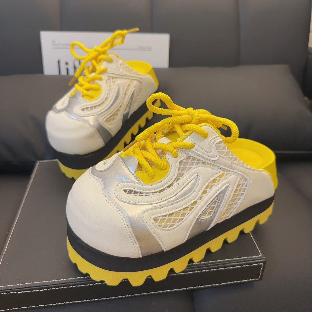 A pair of chunky platform sneakers with a vibrant yellow jagged sole, a black midsole, and a white and silver upper with yellow laces