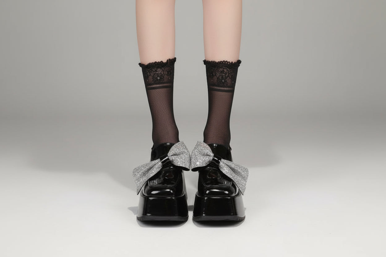 Black platform shoes with silver bows worn by a person on a neutral background