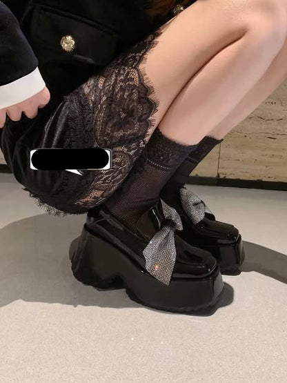 Person wearing black shoes with bows and patterned leggings on a neutral background