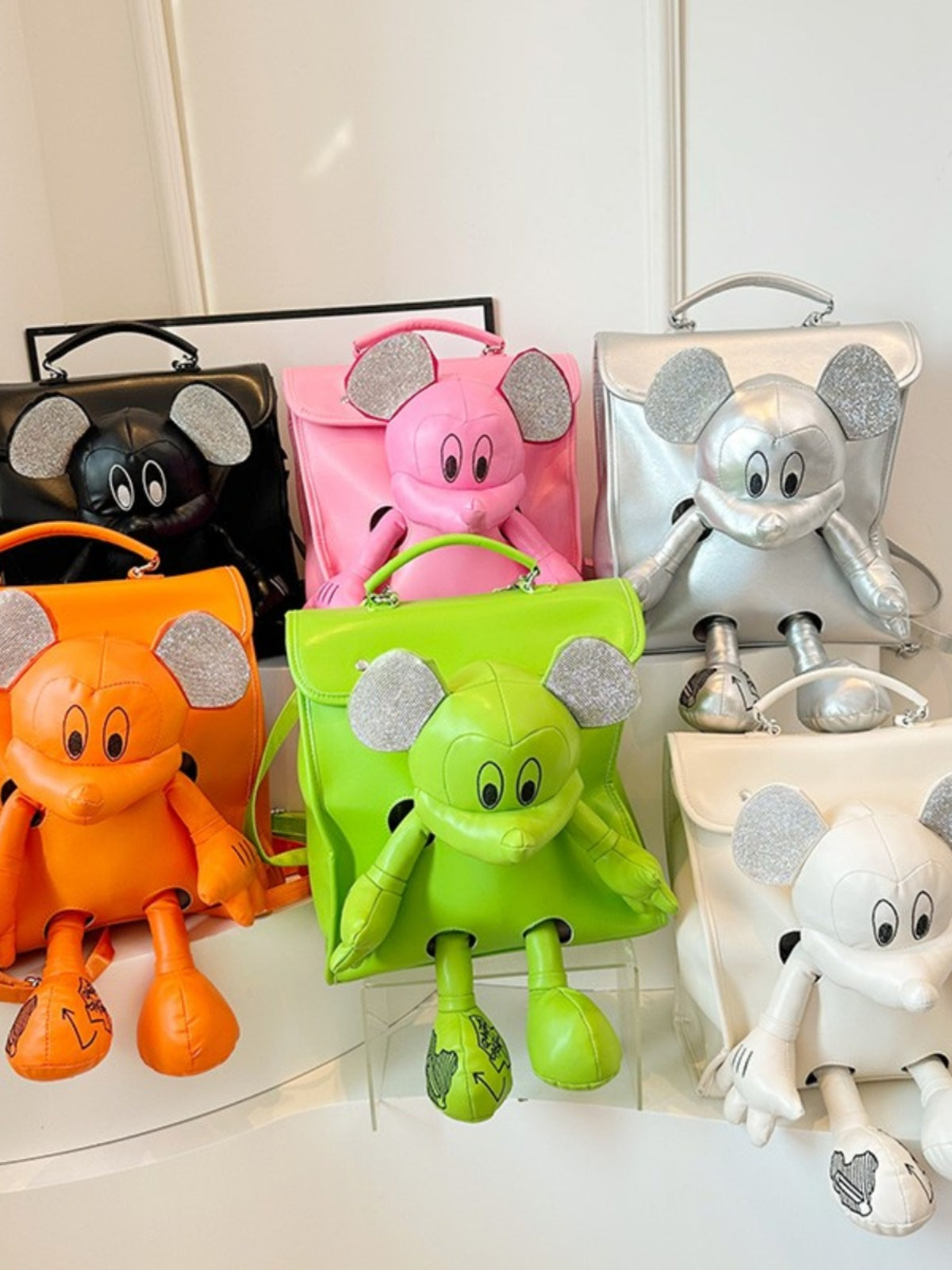 A vibrant collection of six children's backpacks in orange, green, pink, black, silver, and white, 