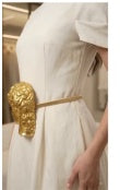 Side detail of gold sculpted buckle belt on ivory dress