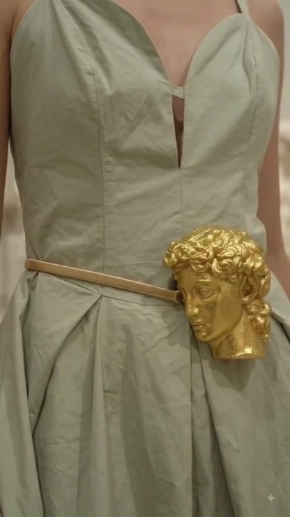 Close-up of gold sculpted face buckle belt on sage green dress