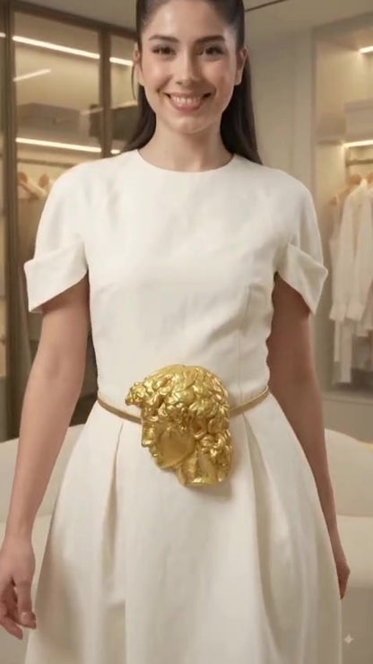 Model in ivory dress wearing gold sculpted face buckle belt — front view